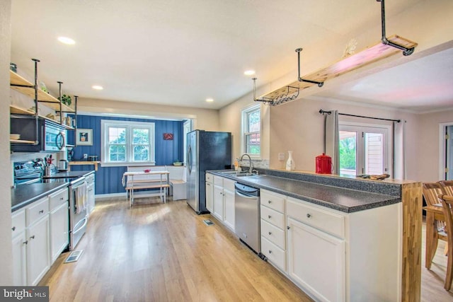 kitchen with dark countertops, appliances with stainless steel finishes, light wood-style floors, white cabinets, and a sink