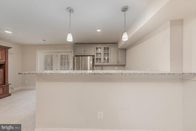 kitchen featuring light stone counters, hanging light fixtures, and stainless steel refrigerator