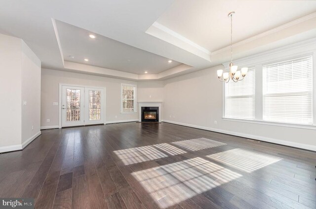 unfurnished living room with a raised ceiling, a chandelier, and dark hardwood / wood-style flooring