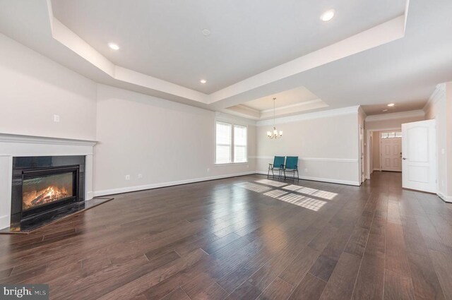 unfurnished living room with crown molding, a chandelier, dark hardwood / wood-style flooring, and a tray ceiling