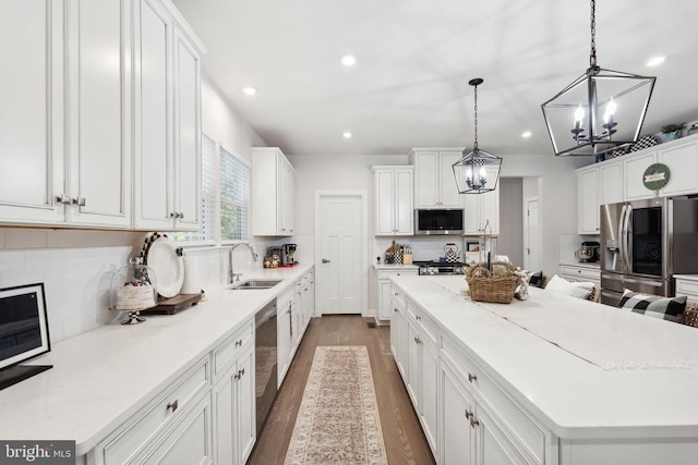 kitchen featuring a large island, a sink, backsplash, white cabinetry, and appliances with stainless steel finishes