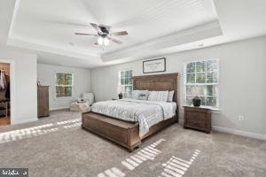 bedroom featuring a tray ceiling, multiple windows, and baseboards