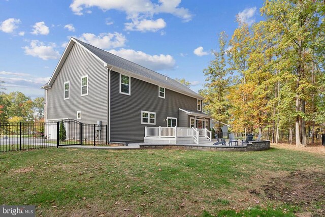 rear view of property with a wooden deck, a patio, a lawn, and fence