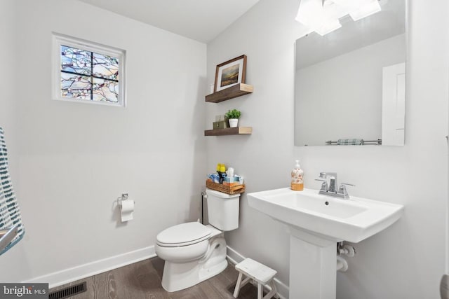 half bathroom with visible vents, toilet, a sink, wood finished floors, and baseboards