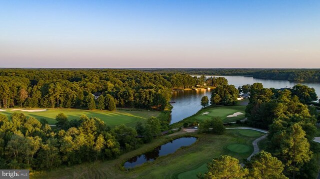 aerial view at dusk with a view of trees, golf course view, and a water view