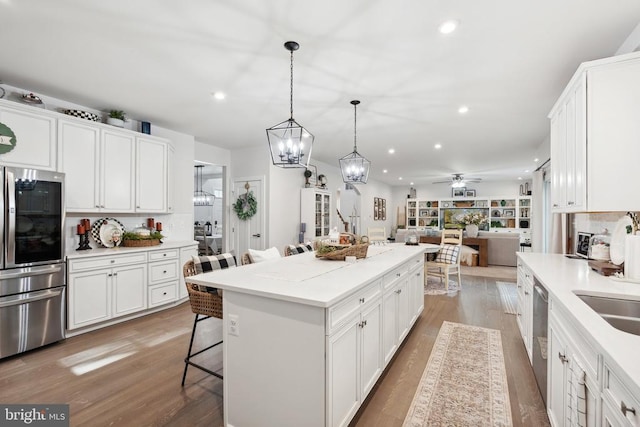 kitchen with stainless steel appliances, white cabinets, ceiling fan with notable chandelier, open floor plan, and a center island