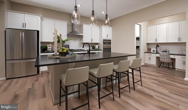 kitchen with appliances with stainless steel finishes, built in desk, white cabinetry, sink, and a center island with sink