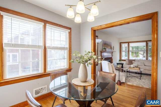 dining area with a fireplace, wood finished floors, visible vents, and a notable chandelier