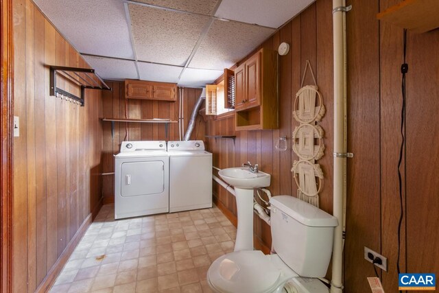 clothes washing area with wooden walls, laundry area, a sink, independent washer and dryer, and light floors