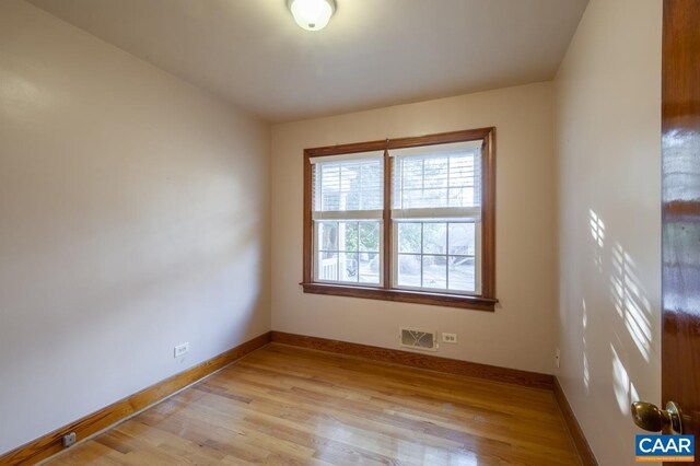 spare room with light wood finished floors, visible vents, and baseboards