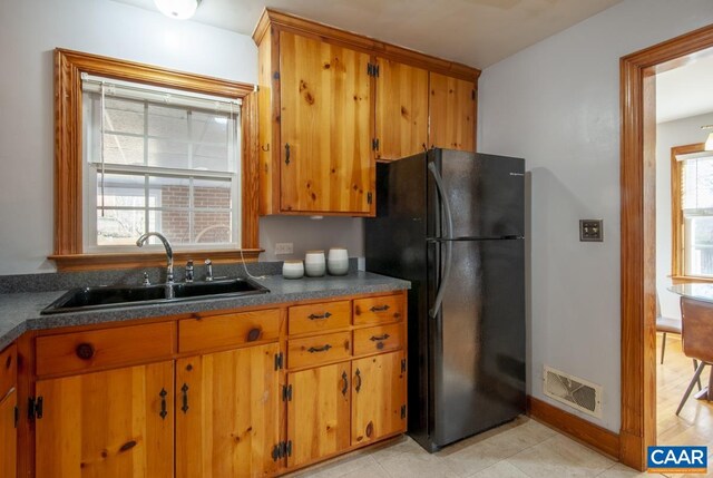 kitchen featuring visible vents, brown cabinetry, dark countertops, freestanding refrigerator, and a sink