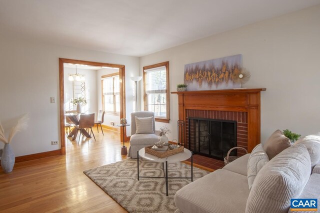 living area with a fireplace, baseboards, a chandelier, and wood finished floors