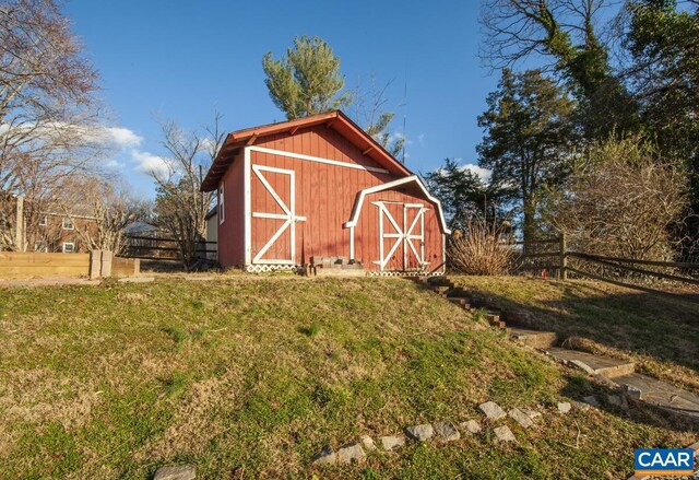 view of barn featuring fence and a lawn