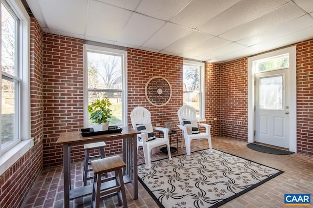 home office featuring brick floor, a drop ceiling, and brick wall