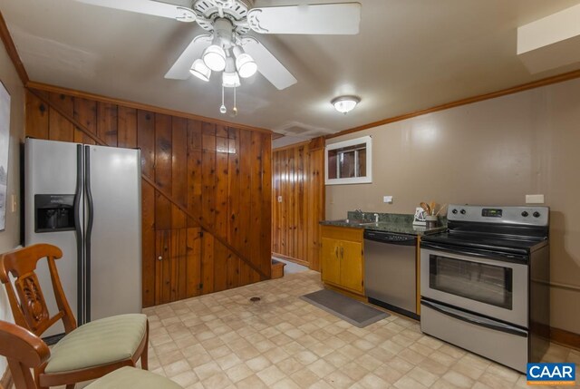 kitchen with light floors, stainless steel appliances, ornamental molding, a ceiling fan, and wooden walls