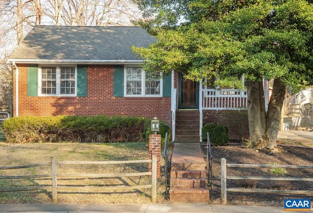 view of front of home with a fenced front yard, a porch, a shingled roof, and brick siding