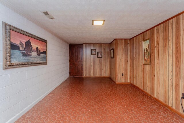 empty room with crown molding, wooden walls, and a textured ceiling