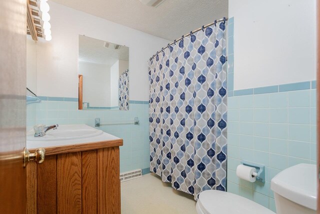 bathroom with vanity, toilet, a textured ceiling, and tile walls