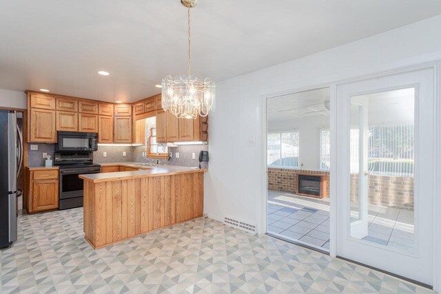 kitchen with sink, stainless steel appliances, a fireplace, decorative backsplash, and kitchen peninsula