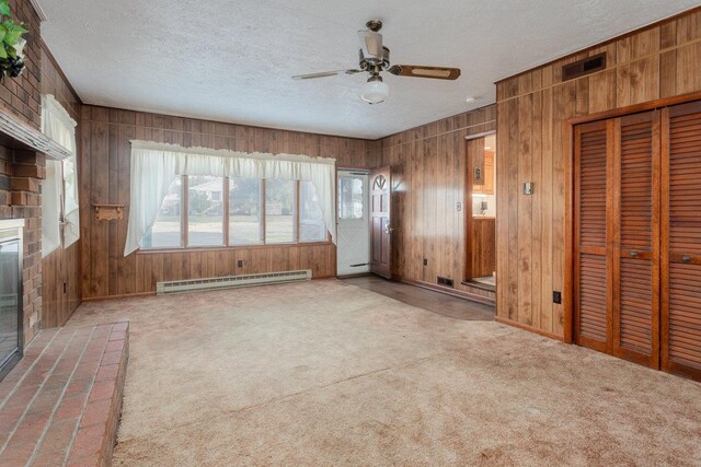 unfurnished living room featuring wood walls, a baseboard radiator, carpet, ceiling fan, and a textured ceiling