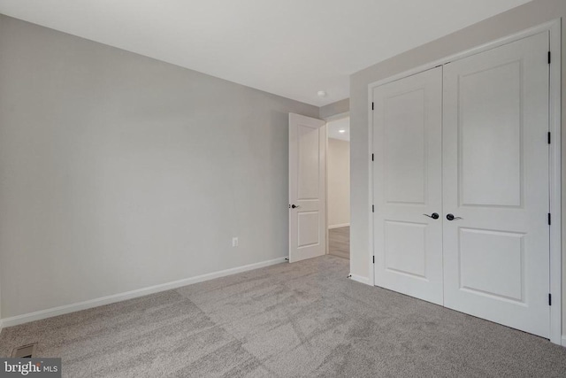 unfurnished bedroom featuring a closet, light colored carpet, and baseboards