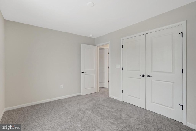 unfurnished bedroom featuring light carpet, a closet, and baseboards