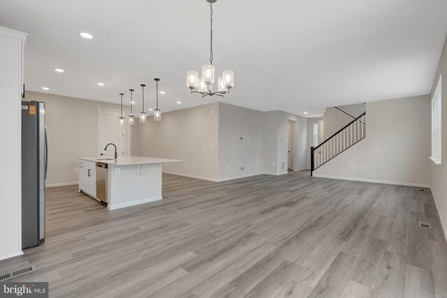 kitchen featuring light countertops, hanging light fixtures, appliances with stainless steel finishes, open floor plan, and a kitchen island with sink