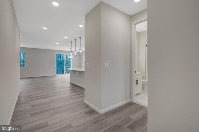 hall with a chandelier, light wood finished floors, recessed lighting, and baseboards