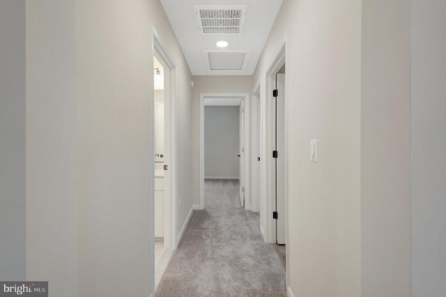 hall with light carpet, baseboards, visible vents, and attic access