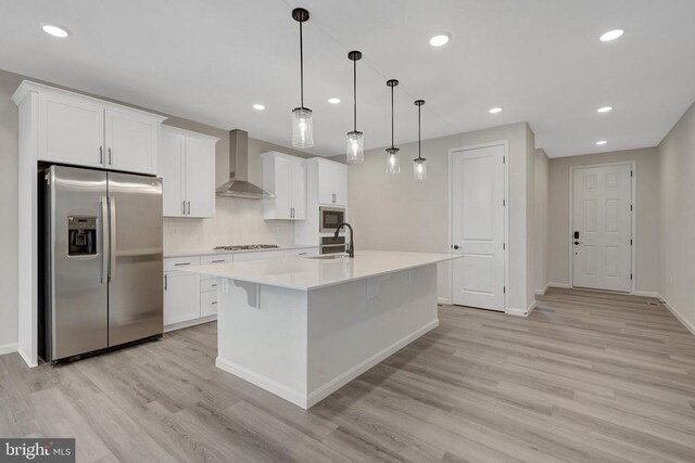 kitchen featuring stainless steel fridge with ice dispenser, an island with sink, wall chimney exhaust hood, light countertops, and pendant lighting