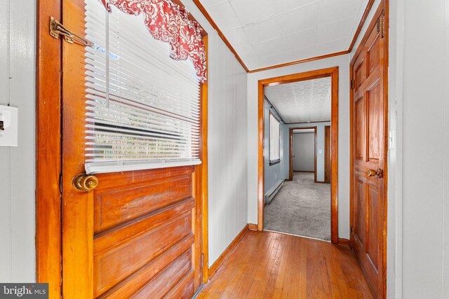 hallway with light wood-type flooring, ornamental molding, and baseboard heating