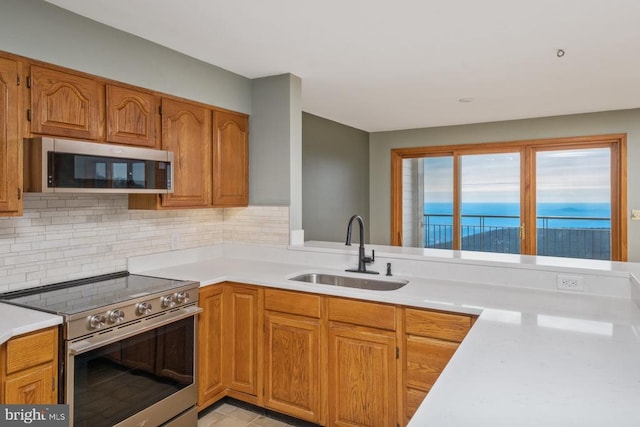 kitchen with decorative backsplash, appliances with stainless steel finishes, brown cabinets, light countertops, and a sink