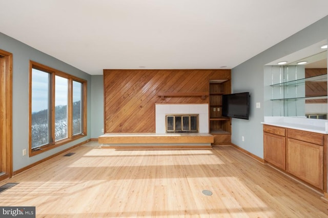 unfurnished living room featuring a glass covered fireplace, visible vents, wood walls, and light wood-style flooring