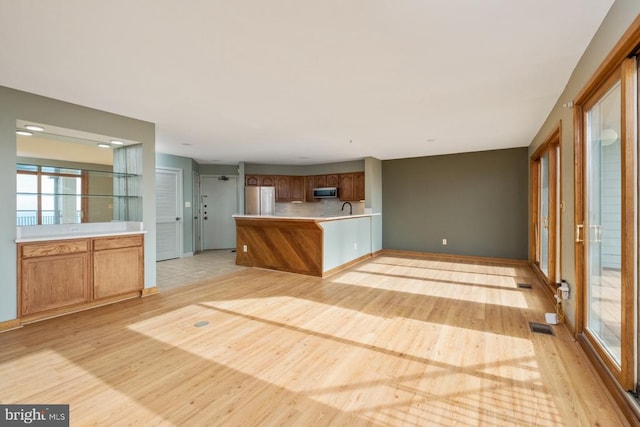 kitchen with light wood finished floors, a peninsula, stainless steel appliances, light countertops, and a sink