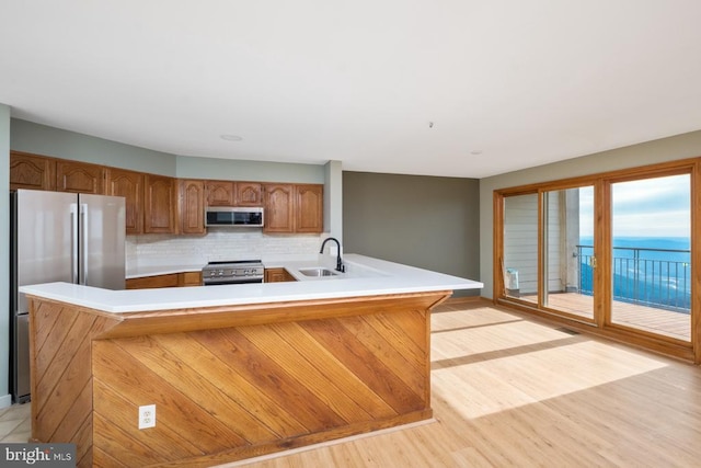 kitchen featuring light wood-style flooring, a sink, light countertops, appliances with stainless steel finishes, and decorative backsplash