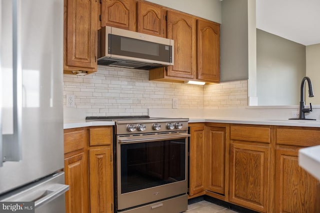 kitchen with appliances with stainless steel finishes, brown cabinetry, and light countertops