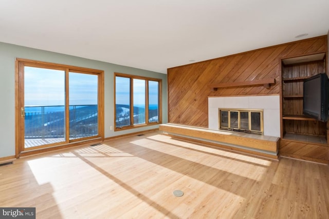 unfurnished living room with wood walls, a fireplace, wood finished floors, visible vents, and baseboards