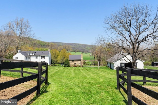 view of yard featuring fence, an outdoor structure, and a rural view