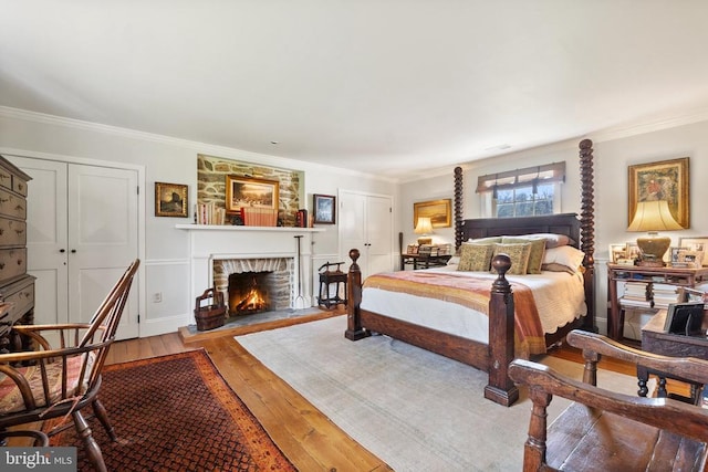 bedroom with crown molding, light wood finished floors, and a warm lit fireplace