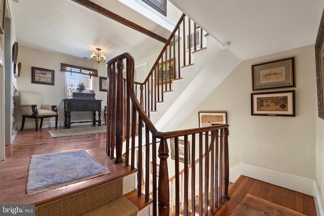 staircase with wood finished floors, a notable chandelier, and baseboards