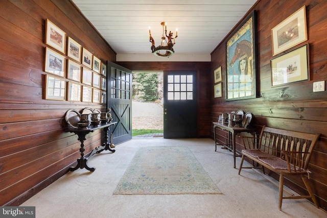 carpeted entrance foyer with wood walls and an inviting chandelier