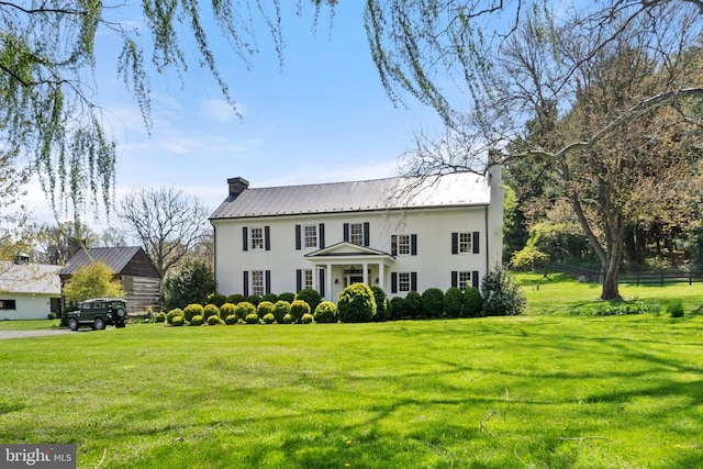 colonial inspired home with stucco siding, a chimney, metal roof, and a front lawn