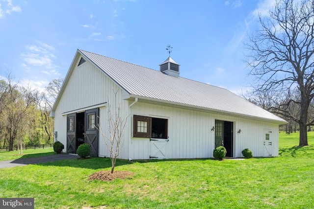 exterior space featuring a standing seam roof, metal roof, an outbuilding, a lawn, and fence