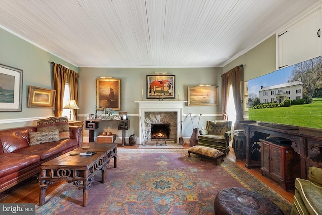 living area with wood finished floors, ornamental molding, and a warm lit fireplace