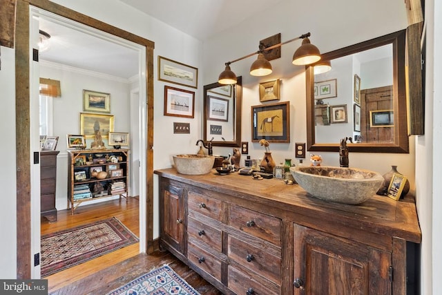 full bathroom with double vanity, hardwood / wood-style floors, crown molding, and a sink