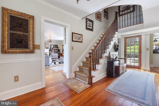 interior space with crown molding, baseboards, wood-type flooring, a notable chandelier, and stairs