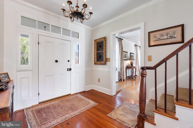 entryway featuring stairway, a chandelier, wood-type flooring, crown molding, and baseboards
