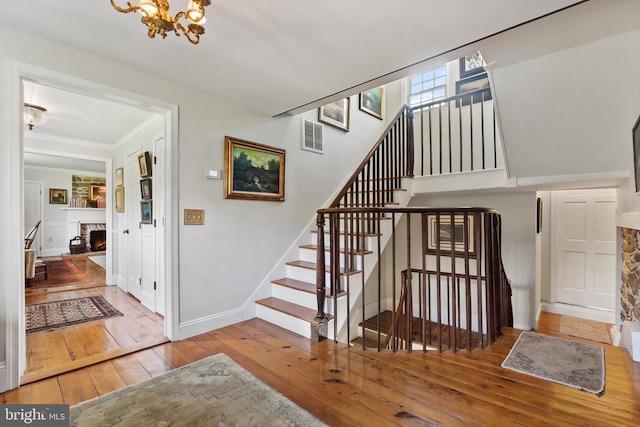 stairs featuring an inviting chandelier, hardwood / wood-style floors, a fireplace, baseboards, and crown molding