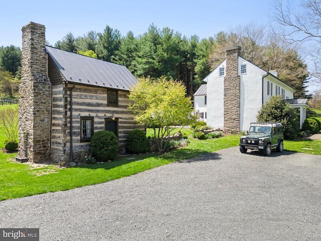 view of side of home featuring a chimney, driveway, metal roof, and a lawn