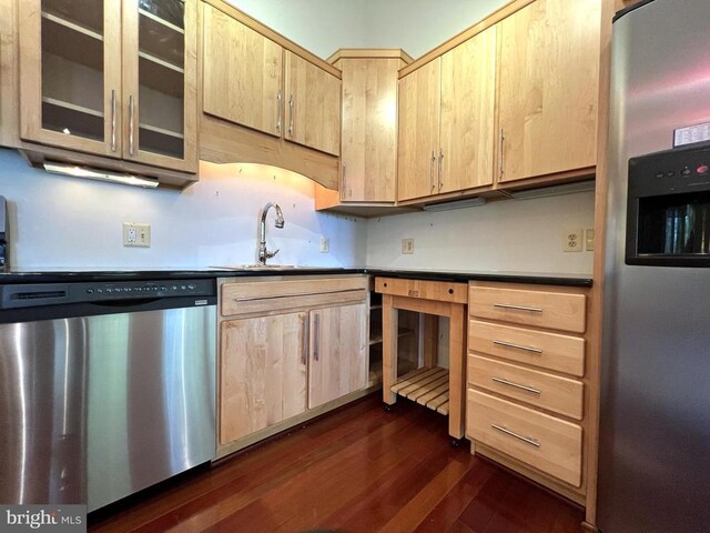 kitchen featuring light brown cabinets, a sink, dark wood-type flooring, glass insert cabinets, and appliances with stainless steel finishes